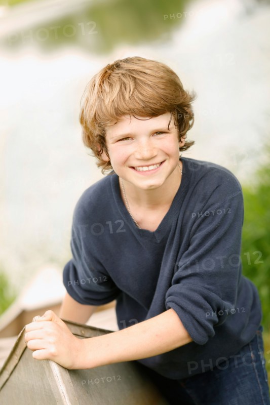 Boy (12-13) posing with boat on grass near lake
