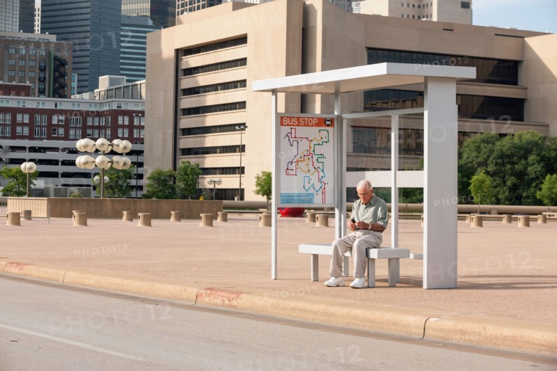Senior man sitting at bus stop and text messaging