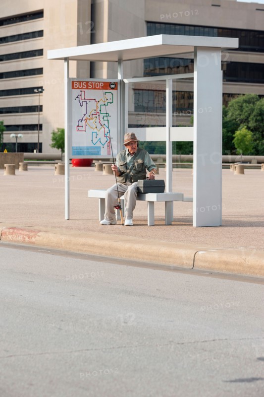 Senior man sitting at bus stop with fishing rod