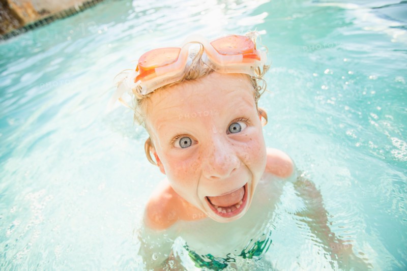 Boy (4-5) swimming in swimming pool and making funny face