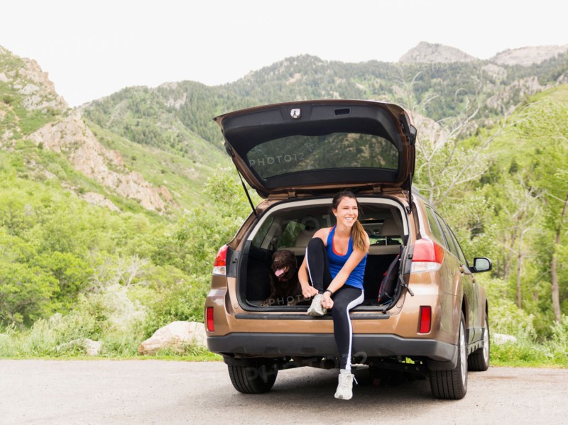 Woman wearing sportswear sitting at car trunk with dog