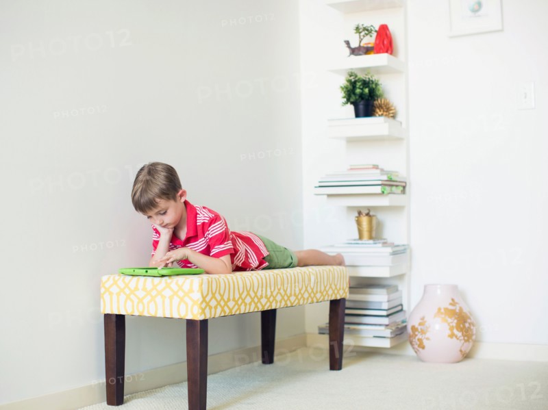 Boy (6-7) lying on bench using digital tablet