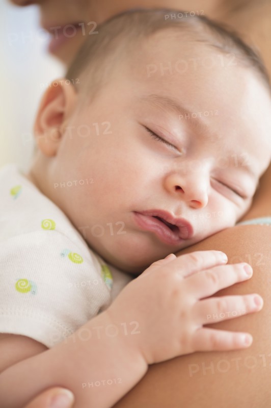 Baby boy (2-5 months) sleeping on mother's shoulder.