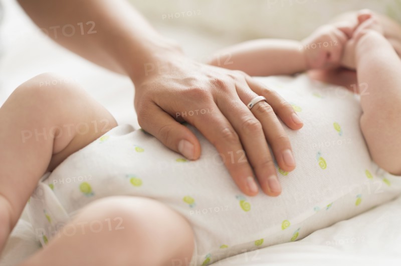 Mother massaging belly of baby boy (2-5 months).