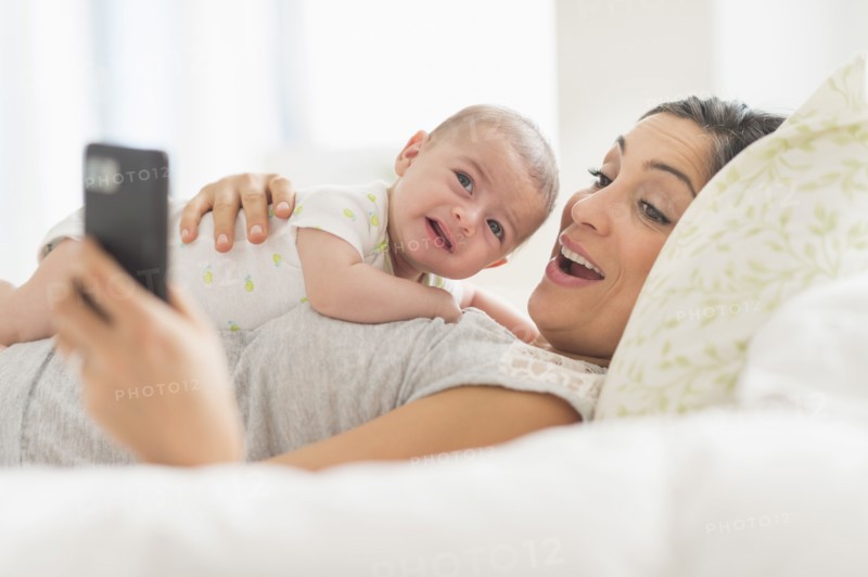 Mother photographing herself and baby boy (2-5 months) with cell phone.