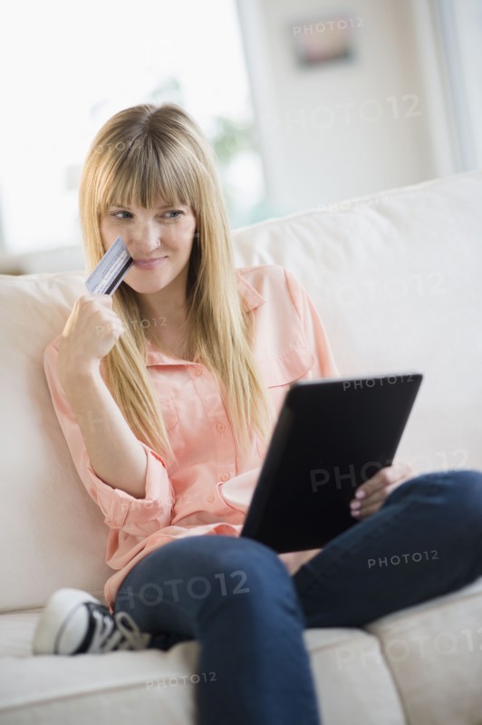 Woman sitting on sofa holding credit card and tablet pc.
Photo : Jamie Grill