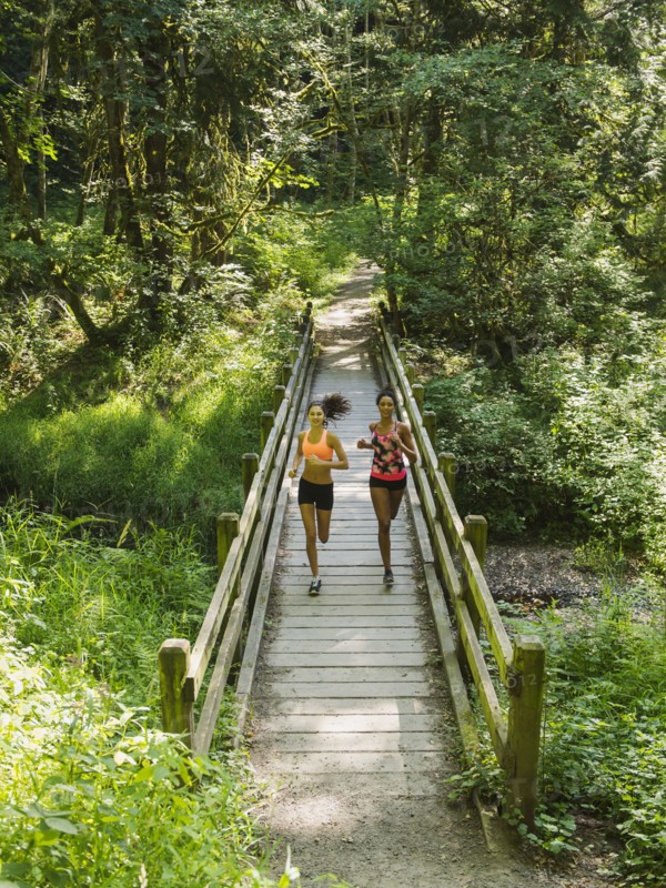 Two young women running over wooden footbridge. USA, Oregon, Portland.