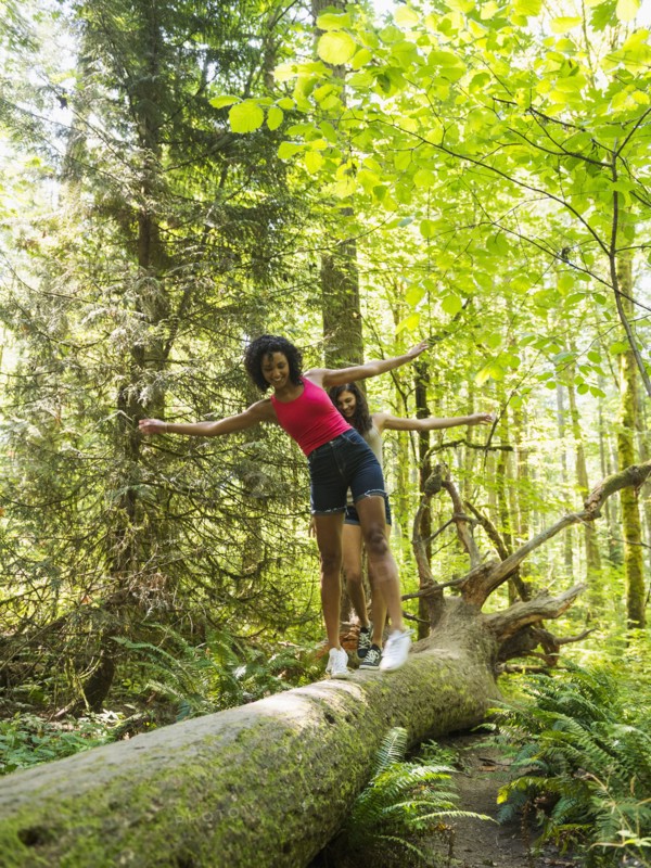 Two young women walking on log in forest. USA, Oregon, Portland.
