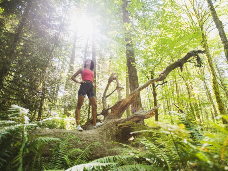 Young woman standing on log in forest. USA, Oregon, Portland.