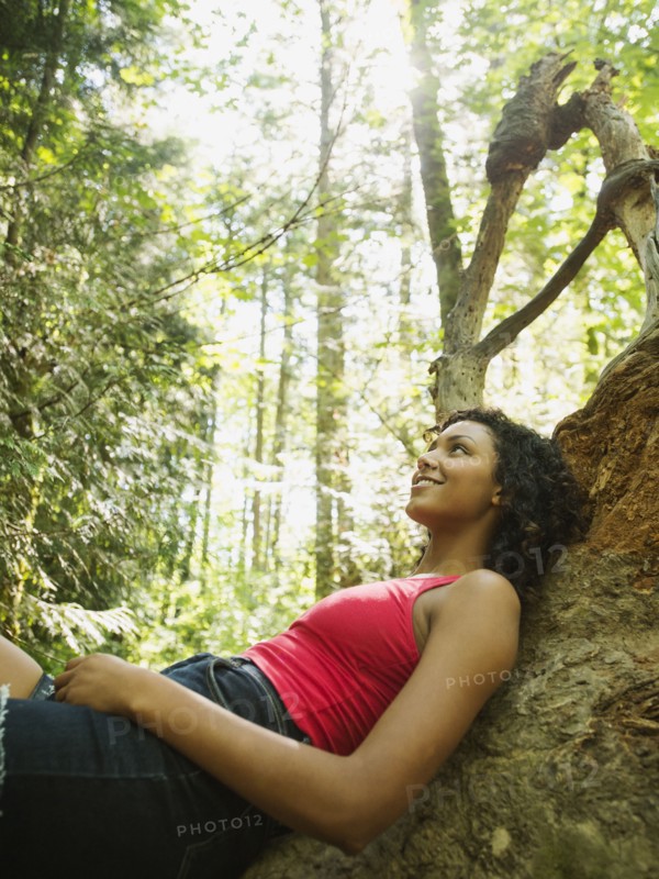 Young woman sitting on log in forest. USA, Oregon, Portland.