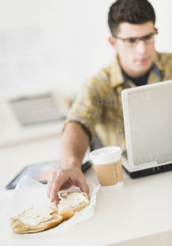 Young man eating sandwich and using laptop.