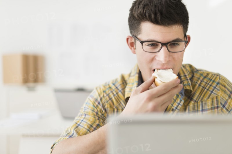Young man eating sandwich and using laptop.
