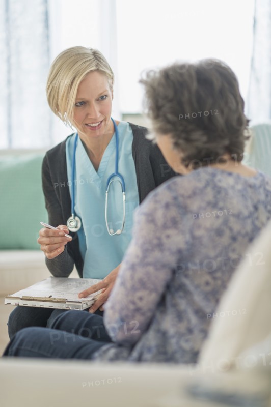 Nurse and mature woman sitting on sofa.