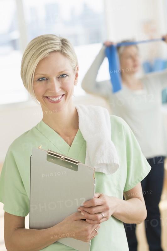 Portrait of personal trainer, mature woman exercising in background.