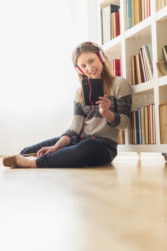 Young woman sitting on floor and listening to music on digital tablet.