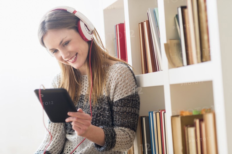 Young woman sitting on floor and listening to music on digital tablet.