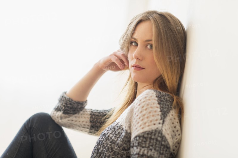 Portrait of attractive young woman sitting by wall.