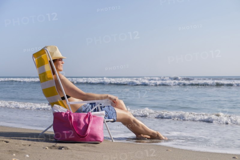 Woman sitting on deckchair on beach.