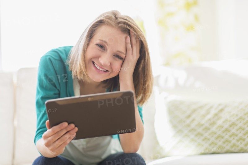 Portrait of woman on sofa holding digital tablet.