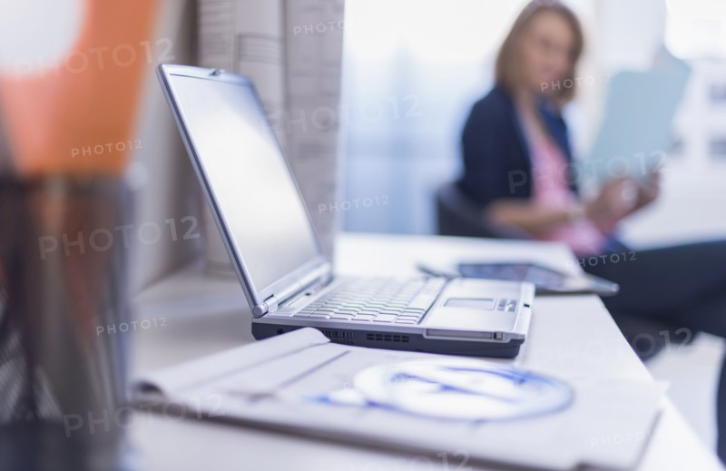 Close up of laptop and digital tablet on desk, woman in background.
