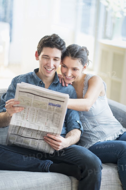 Couple reading newspaper on sofa.