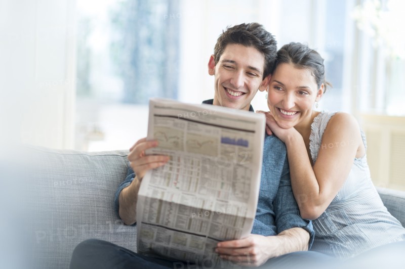 Couple reading newspaper on sofa.