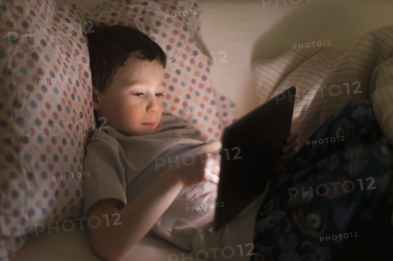 boy (6-7) using digital tablet in bed.