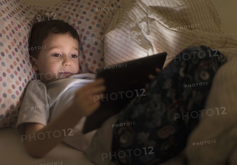 boy (6-7) using digital tablet in bed.