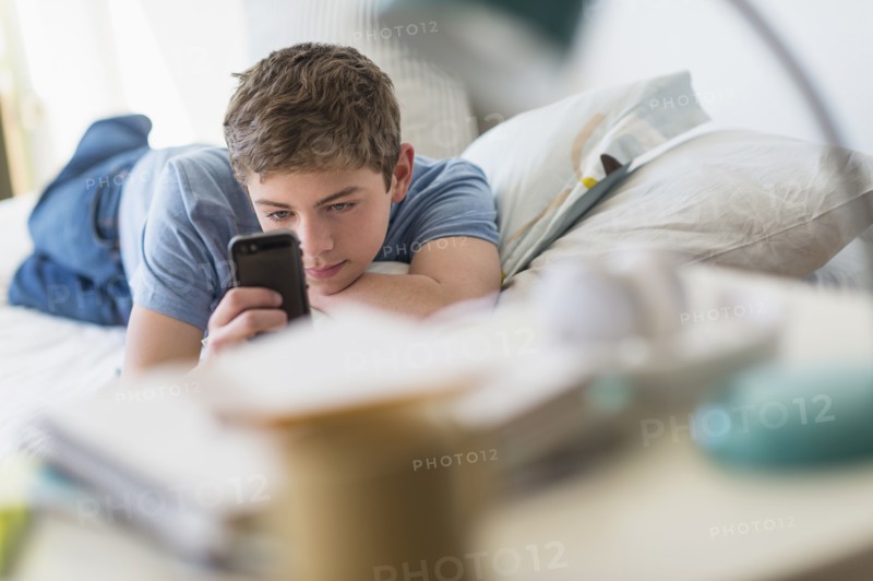 Teenage boy (16-17) lying on bed and text messaging.