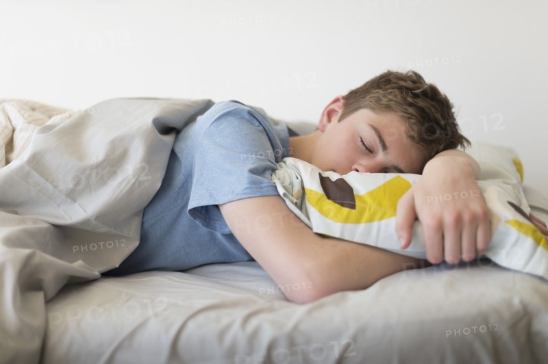 Teenage boy (16-17) sleeping in bed.