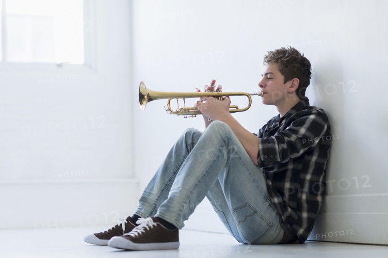 Teenage boy (16-17) playing trumpet in hallway.