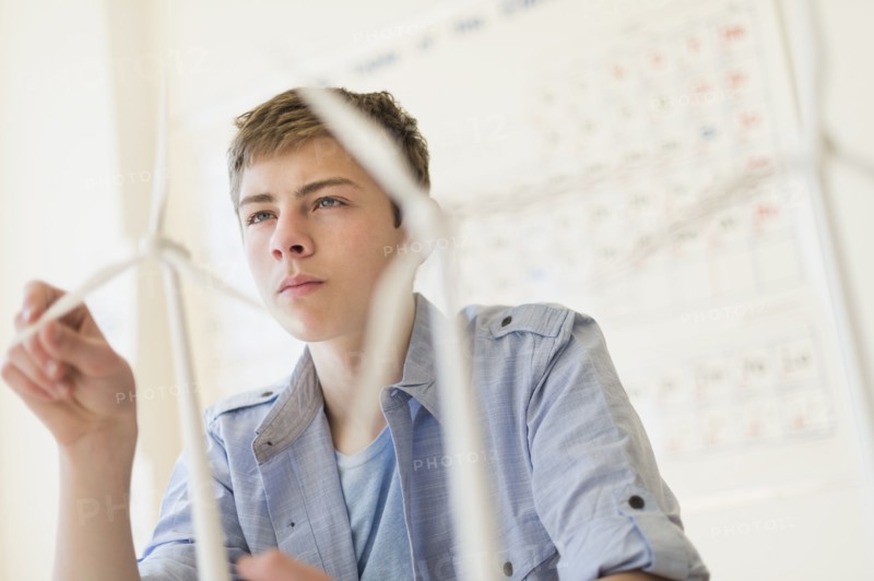 Teenage boy (16-17) touching wind turbines models.