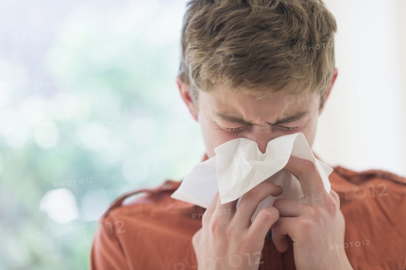 Teenage boy (16-17) blowing nose.