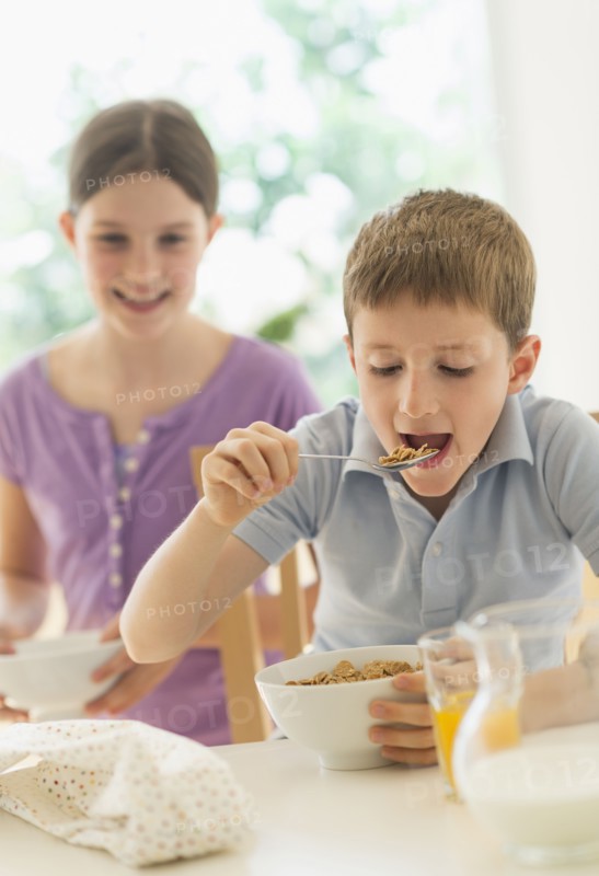 Boy and girl (8-9, 10-11) eating cereals.