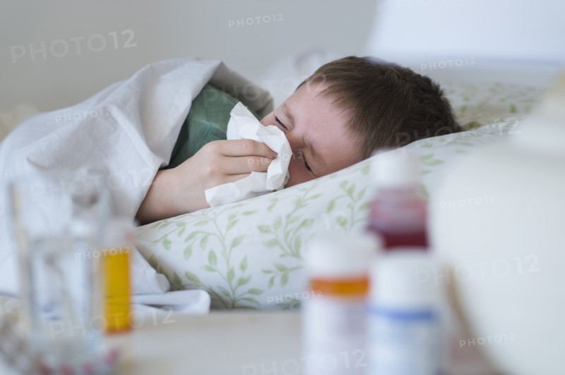 boy (8-9) lying in bed and blowing nose.