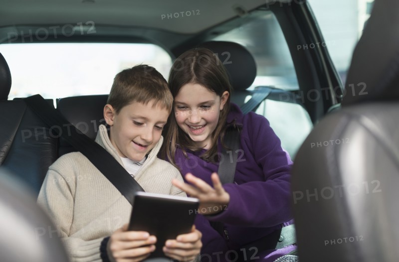 Boy and girl (8-9, 10-11) using digital tablet in car.
