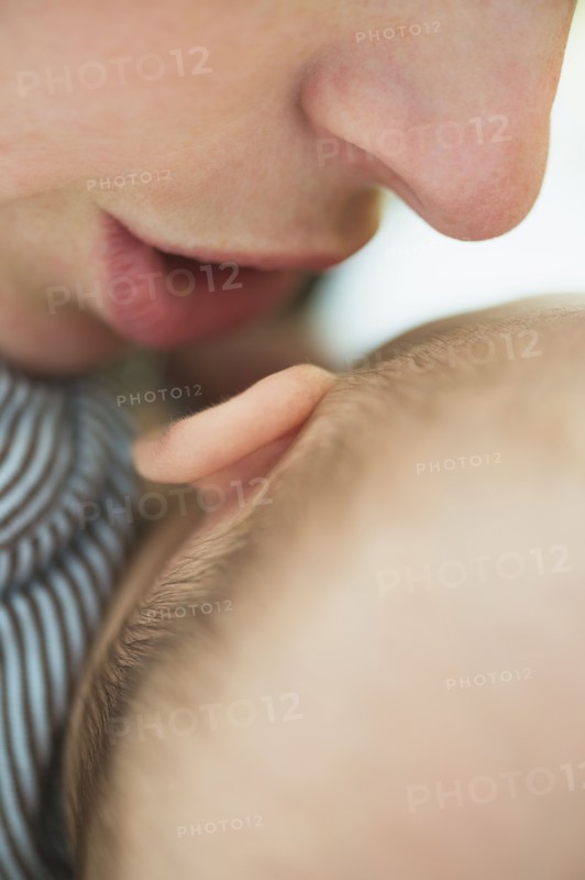 Close up of mother's mouth whispering into baby boy's(2-5 months) ear.