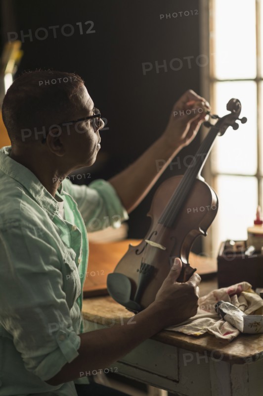 Mature man fixing violin in his workshop.