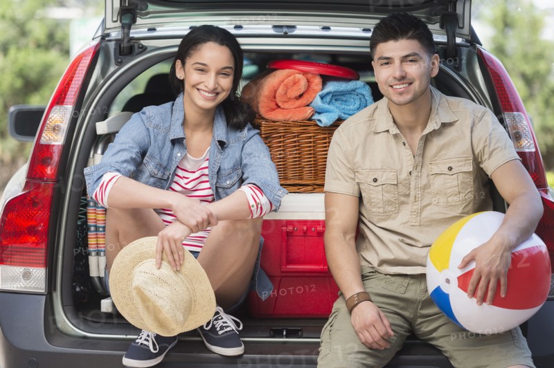 Portrait of young couple sitting in open car trunk.