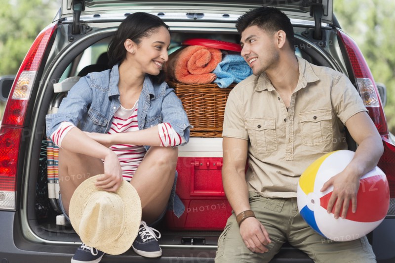 Young couple sitting in open car trunk.