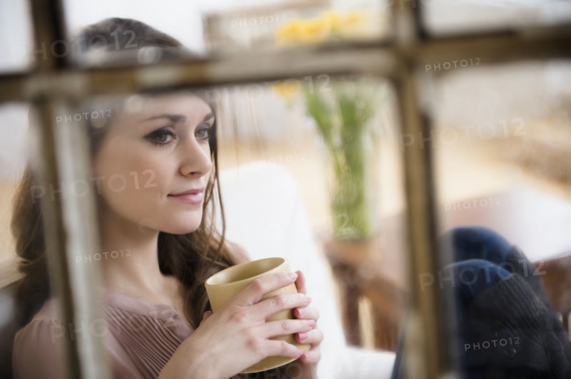 Young woman contemplating in living room with coffee cup in hands.
Photo : Jamie Grill