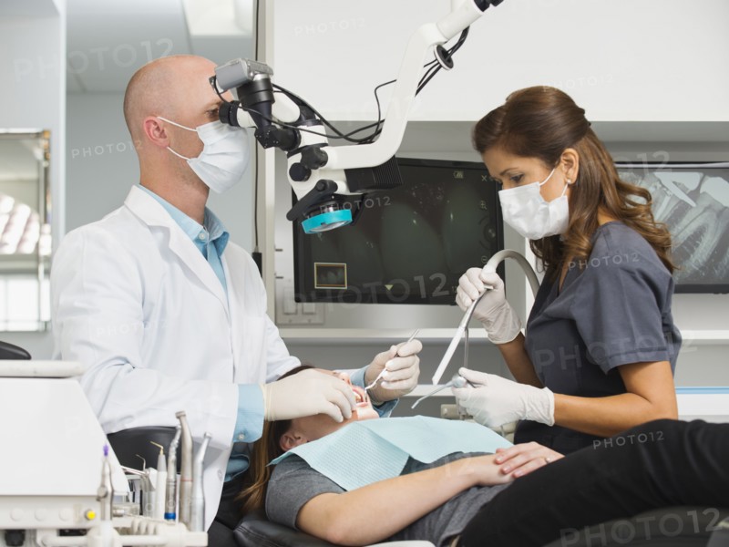 Dentist operation on patient and using microscope.