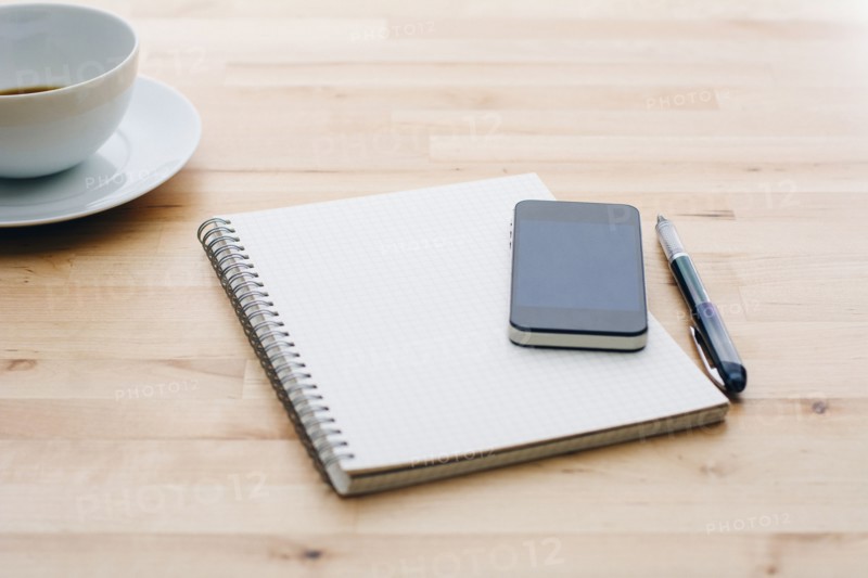 Spiral notebook, Ballpoint pen, Mobile phone and coffee cup on wooden table.
Photo : Kristin Lee