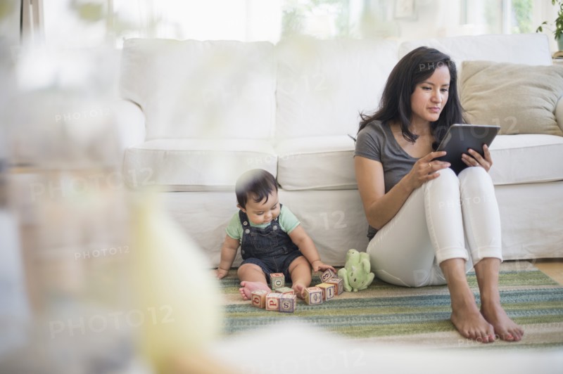 Mother using tablet pc while her son (6-11 months) playing with building blocks.
