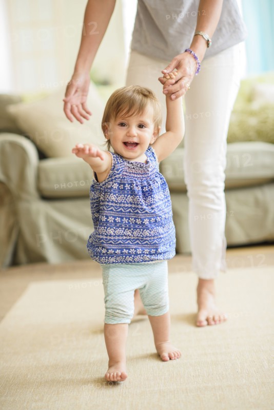Mother assisting baby daughter (18-23 months) with her first steps.