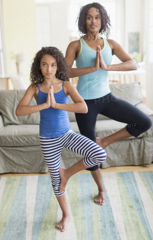 Mother and daughter (8-9) doing in yoga poses in living room.
