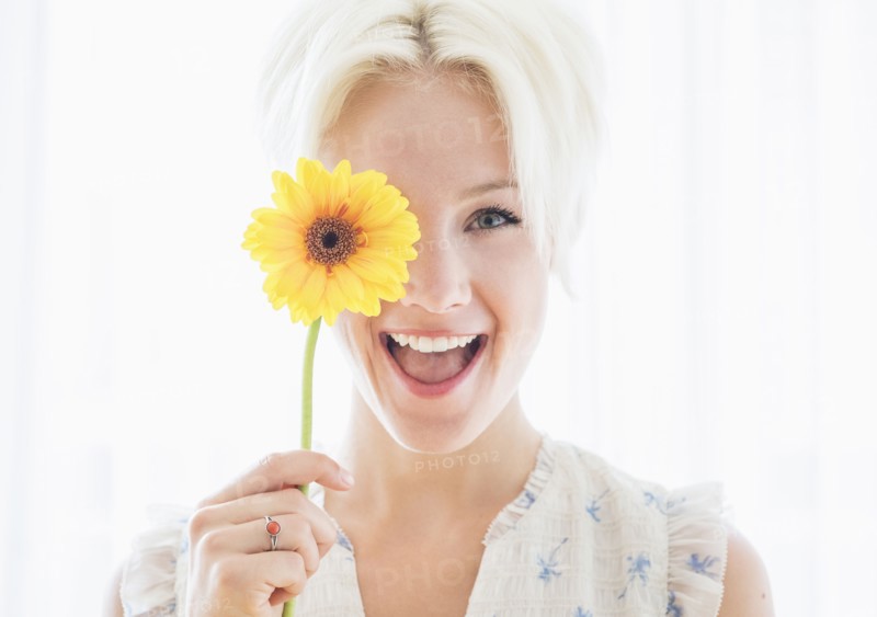 Portrait of blonde woman holding yellow flower.