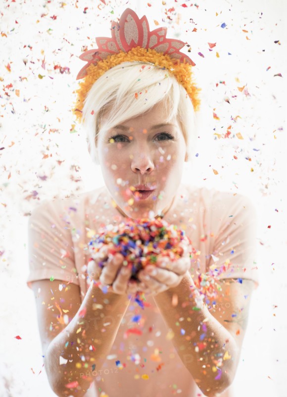 Woman wearing tiara blowing confetti.
