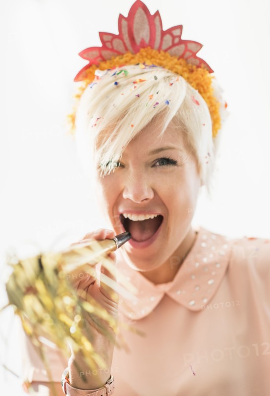 Woman wearing tiara blowing party horn blower.