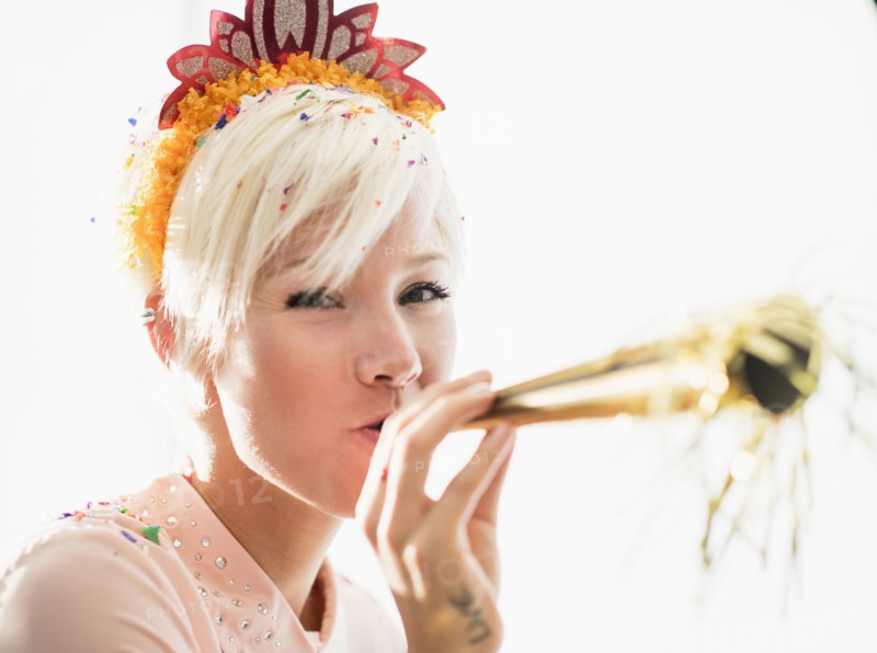 Woman wearing tiara blowing party horn blower.